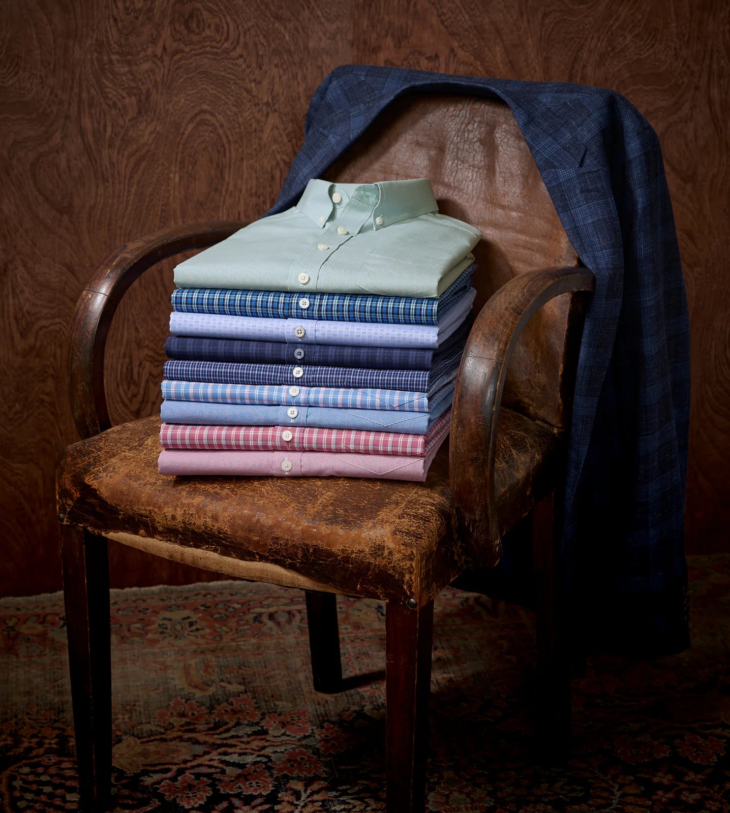 A stack of shirts on a chair with a jacket draped over it.